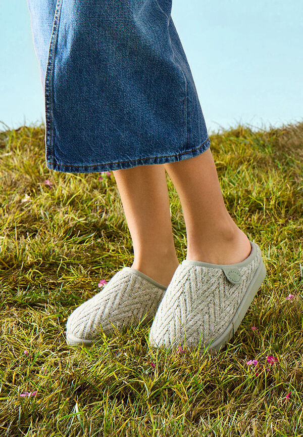 Light green knit mule slippers worn with a denim skirt while standing in a grassy field.