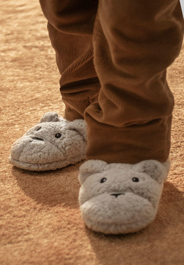 Gray plush bear slippers worn with brown corduroy pants on a soft carpet.