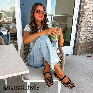 Woman wearing leopard print ballet flats while enjoying an iced drink on a sunny patio.