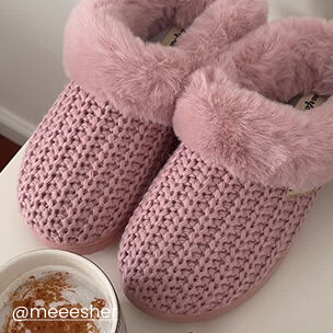 Pair of pink knit slippers with plush faux-fur lining beside a cup of coffee.