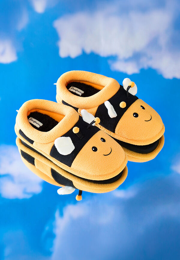 Plush bee-shaped slippers with smiling faces and soft wings reflected on a glossy surface against a sky-blue backdrop.