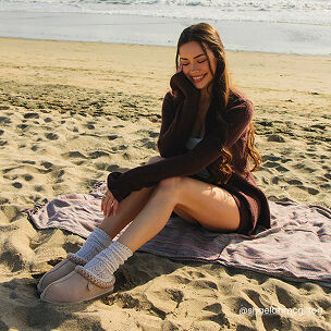 Woman relaxing on the beach wearing cream Fireside clogs with cozy knit socks.