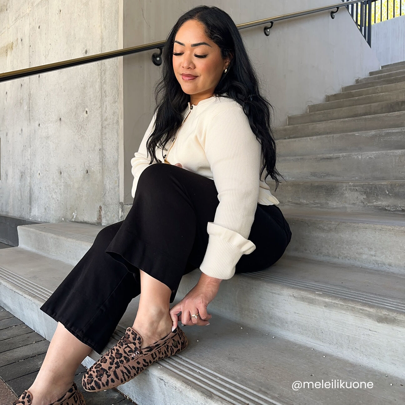 Woman sitting on concrete stairs wearing a cream ribbed sweater, black pants, and leopard-print slip-on loafers.